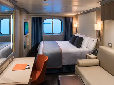 Eine modern eingerichtete Außenkabine an Bord der Koningsdam mit Doppelbett, Sofa, Schreibtisch und einem großen Fenster mit Blick auf das Meer.