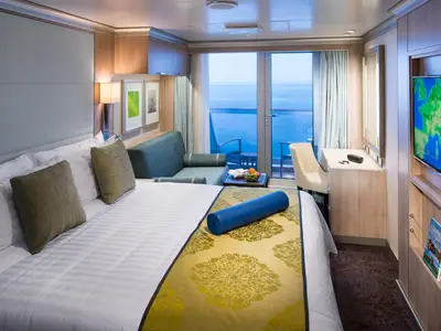 Hell eingerichtete Balkonkabine an Bord der Koningsdam mit einem Doppelbett, einer Yogamatte, Sofa und Meerblick.