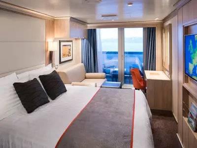 Einladende Balkonkabine an Bord der Koningsdam mit Doppelbett, Sofa, Schreibtisch und Blick auf das Meer.