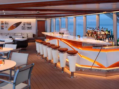 Die stilvolle Sea View Bar an Bord der Koningsdam mit Barhockern vor einer geschwungenen Theke und Panoramafenstern zum Meer.