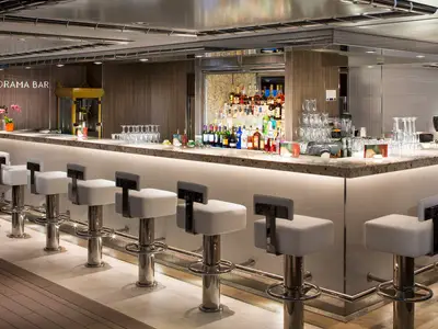 Die elegante Panorama Bar an Bord der Koningsdam mit weißen Barhockern und einer beleuchteten Theke.