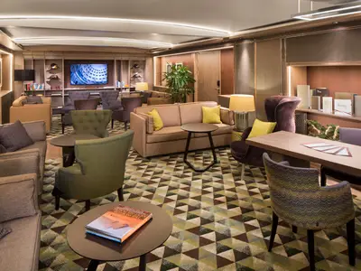 Die gemütliche Neptune Lounge an Bord der Koningsdam bietet stilvolle Sitzgelegenheiten auf einem gemusterten Teppich.