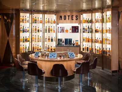 Die edle Whiskey-Bar 'Notes' an Bord der Koningsdam mit einer großen Flaschenauswahl und einem runden Verkostungstisch mit Barhockern.