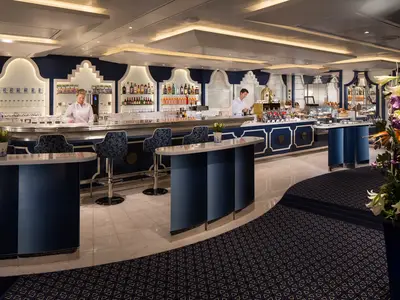 Das stilvolle Grand Dutch Cafe an Bord der Koningsdam mit blau-weißer Einrichtung, Barhockern und Crew-Mitgliedern hinter dem Tresen.
