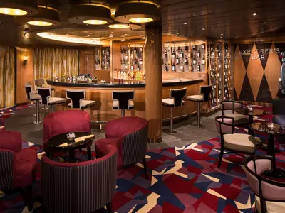 Blick in die stilvolle Explorer's Bar an Bord der Koningsdam mit roten Sesseln und einer eleganten Bar.