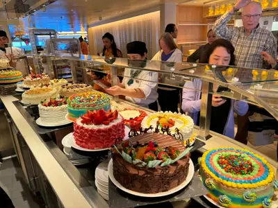 Gäste und Crew-Mitglieder stehen an Bord der Koningsdam vor einer großen Auswahl kunstvoll dekorierter Torten am Buffet.