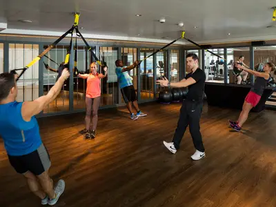 Mehrere Passagiere trainieren an Bord der Koningsdam mit TRX-Bändern im Fitnessbereich, angeleitet von einem Trainer.