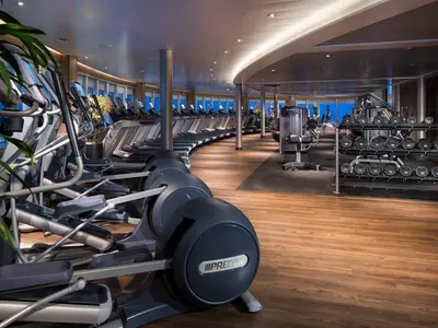 Der großzügige Fitnessraum an Bord der Koningsdam mit modernen Trainingsgeräten, Hanteln und Blick aufs Meer.
