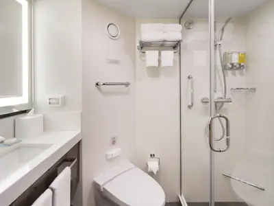 Blick in das helle Badezimmer einer Kabine an Bord der Koningsdam mit einer Glasdusche, Waschbecken und weißen Handtüchern.