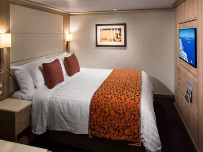 Einladende Innenkabine an Bord der Koningsdam mit gemütlichem Doppelbett, orangefarbenem Bettläufer und einem Flachbildfernseher.