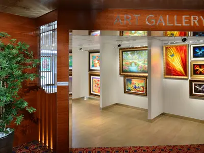 Blick in die helle Kunstgalerie an Bord der Koningsdam mit verschiedenen beleuchteten Gemälden an den Wänden.