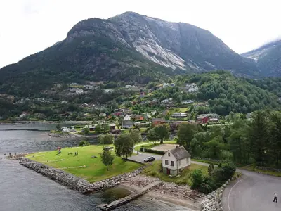 Ein kleiner Ort am Fjord während eines Landausflugs der Koningsdam in Norwegen mit grüner Wiese und Bergen.