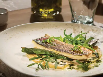 Ein kunstvoll angerichtetes Fischgericht mit grünem Gemüse auf einem weißen Teller an Bord der Koningsdam.