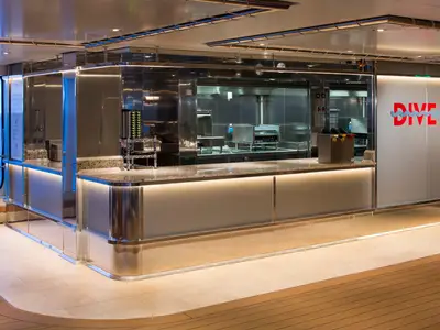 Der moderne Food-Counter 'Dive In' an Bord der Koningsdam mit Edelstahlflächen und Blick aufs Meer im Hintergrund.