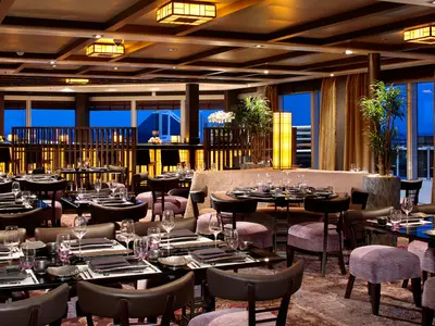 Elegant gedeckte Tische im Restaurant Tamarind an Bord der Koningsdam mit Blick auf das Meer am Abend.