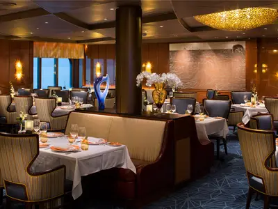 Elegantes Restaurant Pinnacle Grill an Bord der Koningsdam mit weiß gedeckten Tischen, edlen Stühlen und warmer Beleuchtung.