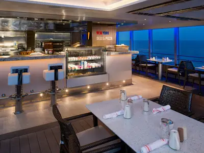 Der gemütliche Gastronomiebereich New York Deli & Pizza an Bord der Koningsdam mit gedeckten Tischen und Blick auf das Meer am Abend.