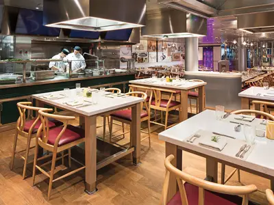 Blick in das stilvolle Culinary Arts Center Restaurant mit Showküche und elegant eingedeckten Holztischen an Bord der Koningsdam.