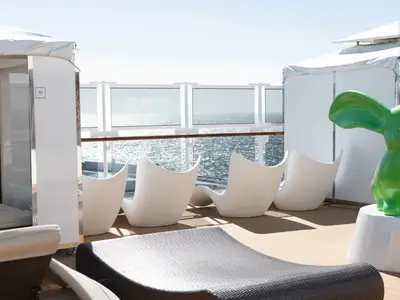 Weiße Liegestühle und eine grüne Hasenskulptur im exklusiven Retreat-Bereich an Bord der Koningsdam mit Blick auf das Meer.