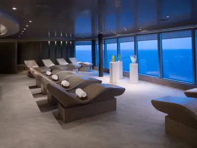 Gemütliche Liegen im Wellnessbereich an Bord der Koningsdam mit Blick durch große Fenster auf das blaue Meer.