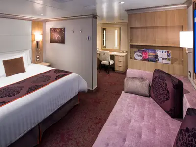 Blick in eine geräumige Signature Suite an Bord der Koningsdam mit einem Doppelbett, einem Sofa im Vordergrund und einer Schreibtischecke im Hintergrund.
