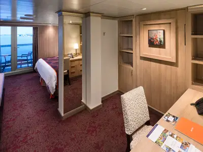 Blick in eine elegante Signature Suite an Bord der Koningsdam mit Holzdekor, einem Arbeitsplatz und Balkonzugang zum Meer.