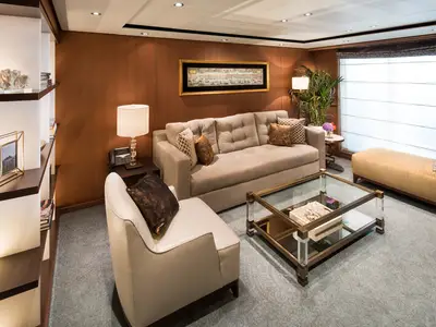Der einladende, elegant eingerichtete Wohnbereich einer luxuriösen Suite an Bord der Koningsdam mit beigen Polstermöbeln und warmem Licht.