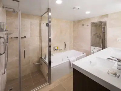 Modernes Badezimmer einer Suite an Bord der Koningsdam mit großer Badewanne, Glasdusche und Waschtisch.