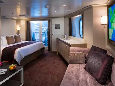 Eine elegant eingerichtete Suite an Bord der Koningsdam mit Doppelbett, Sofa, großem Bildschirm und Blick auf den Balkon.