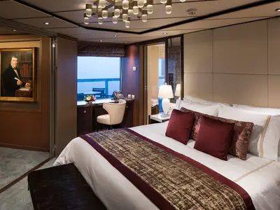 Eine elegant eingerichtete Suite an Bord der Koningsdam mit großem Bett, edlen Textilien und Fenster mit Blick auf das Meer.