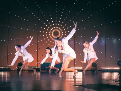 Vier Tänzerinnen in weißen Show-Kostümen bei einer Tanzperformance auf der Bühne an Bord der Koningsdam.