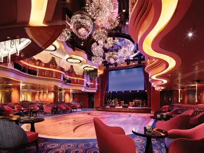 Innenansicht der stilvollen Queen's Lounge an Bord der Koningsdam mit Tanzfläche, roten Sesseln, Discokugeln und einer Bühne.