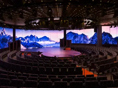 Das moderne Theater World Stage an Bord der Koningsdam mit kreisförmiger Bühne und riesigen LED-Bildschirmen, die schneebedeckte Berge zeigen.