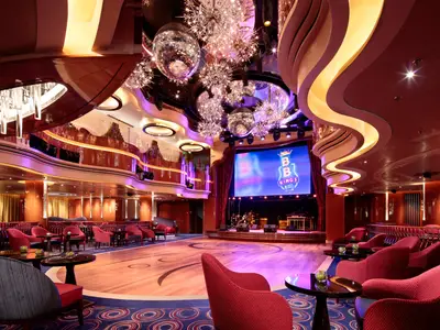 Blick in den eleganten B.B. King's Blues Club an Bord der Koningsdam mit Tanzfläche, roter Bestuhlung, Bühne und Discokugeln.