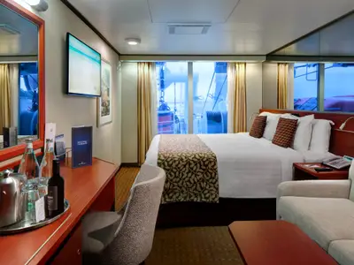 Eine Außenkabine mit eingeschränkter Sicht an Bord der Nieuw Amsterdam, ausgestattet mit Doppelbett, Schreibtisch und Sessel.