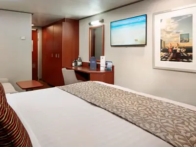 Ein Doppelbett mit gemusterter Decke, ein Schreibtisch, ein Fernseher und ein Bild in einer Kabine an Bord der Nieuw Amsterdam.