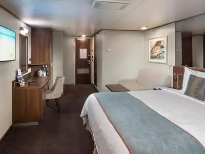 Blick in eine Spa-Außenkabine an Bord der Nieuw Amsterdam mit Doppelbett, Sofa, Schreibtisch und Fernseher.