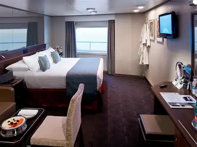 Einladende Außenkabine mit Doppelbett, Schreibtisch und Meerblick durch das Fenster an Bord der Nieuw Amsterdam.