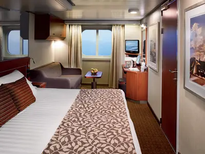 Eine geräumige Außenkabine an Bord der Nieuw Amsterdam mit Doppelbett, Sofa, TV und großem Fenster mit Meerblick.