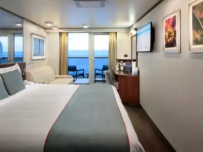 Modern eingerichtete Balkonkabine an Bord der Nieuw Amsterdam mit Doppelbett, Sofa, Schreibtisch und Balkon mit Meerblick.