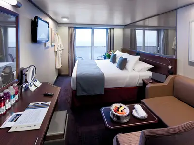 Eine helle und gemütliche Balkonkabine an Bord der Nieuw Amsterdam mit Doppelbett, Sofa, Obstteller auf dem Tisch und Balkonzugang.