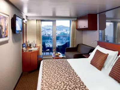 Innenansicht einer eleganten Balkonkabine an Bord der Nieuw Amsterdam mit Bett, Sofa und Balkonausblick.