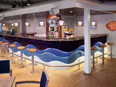 Die moderne Sea View Bar an Bord der Nieuw Amsterdam mit blau-weißem Wellen-Design an der Theke, Barhockern aus Holz und einer Obstschale.