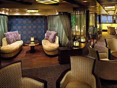 Einblick in die asiatisch gestaltete Silk Den Lounge an Bord der Nieuw Amsterdam mit warmem Licht und gemütlichen Polstermöbeln.