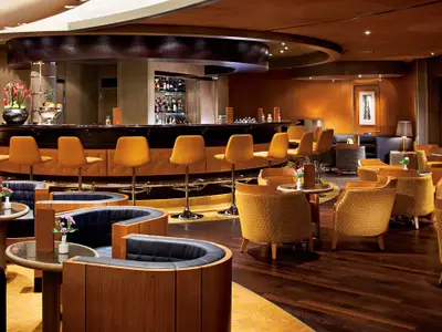 Stilvolle Ocean Bar an Bord der Nieuw Amsterdam mit gelben Barhockern, Sesseln und runden Holzelementen.
