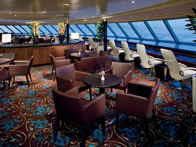 Blick in die gemütliche Crow's Nest Lounge an Bord der Nieuw Amsterdam mit großen Panoramafenstern und bequemen Sesseln.