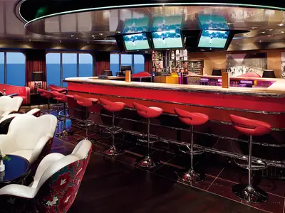 Einladende Casino Bar an Bord der Nieuw Amsterdam mit einer geschwungenen roten Theke, Barhockern, weißen Sesseln und Fenstern zum Meer.