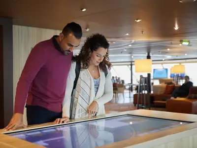 Ein Paar steht an Bord der Nieuw Amsterdam vor einem großen interaktiven Touchscreen-Tisch im Explorations Central.