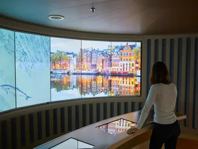 Eine Frau nutzt einen Touchscreen im interaktiven Explorations Central an Bord der Nieuw Amsterdam vor großen Bildschirmen.