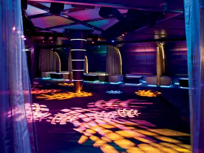 Blick auf die bunt beleuchtete Tanzfläche und gemütliche Sitzecken im Northern Lights Night Club an Bord der Nieuw Amsterdam.